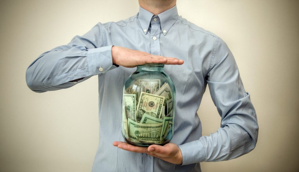 A person holding a jar full of money. This image is featured in the blog post titled, "Will more money make me happier?" written by The Physician Philosopher and featured on the Passive Income, M.D. blog.